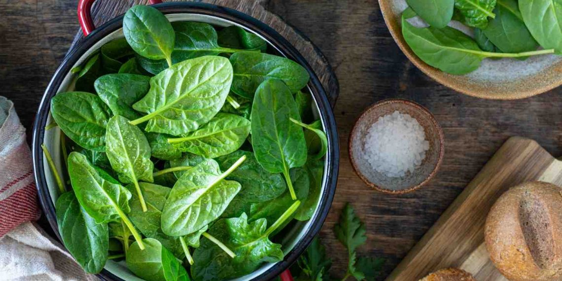 Fresh spinach leaves in a red pot on a wooden table.