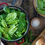 Fresh spinach leaves in a red pot on a wooden table.