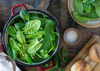 Fresh spinach leaves in a red pot on a wooden table.
