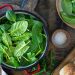 Fresh spinach leaves in a red pot on a wooden table.