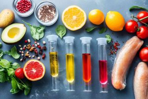 Fresh ingredients and colorful liquids in test tubes on a kitchen surface.