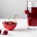 Cherries in red bowl and glass of cherry juice on white table.
