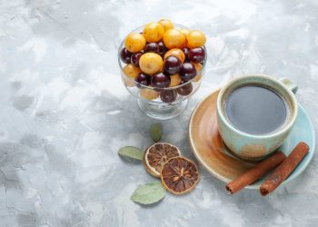 Bowl of yellow and purple berries next to coffee with spices.