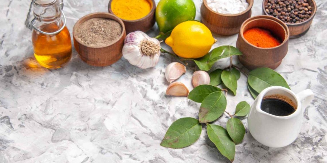 Spices, garlic, and lemons on marble surface with olive oil bottle.