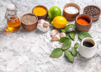 Spices, garlic, and lemons on marble surface with olive oil bottle.