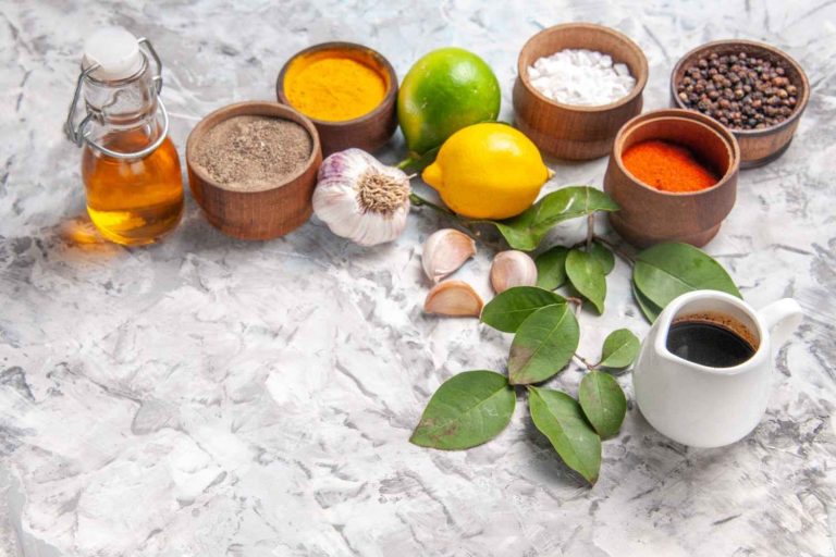 Spices, garlic, and lemons on marble surface with olive oil bottle.