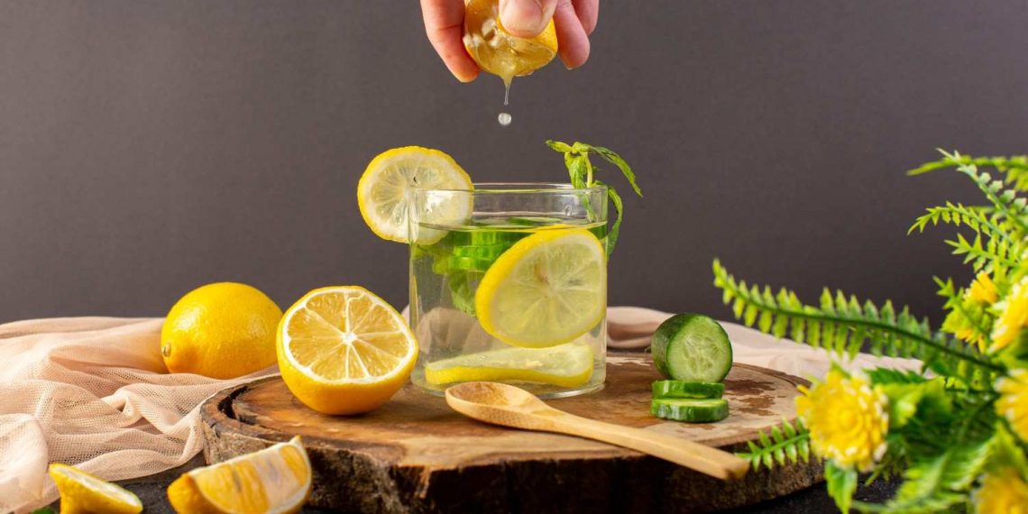 Squeezing lemon into glass with cucumber slices and mint.