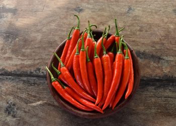 Red chili peppers in a bowl on a rustic wooden background.