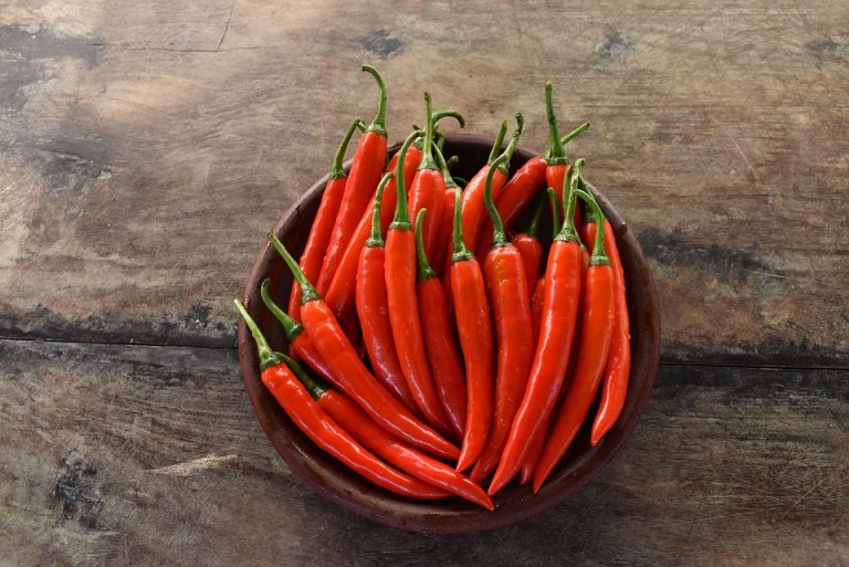 Red chili peppers in a bowl on a rustic wooden background.