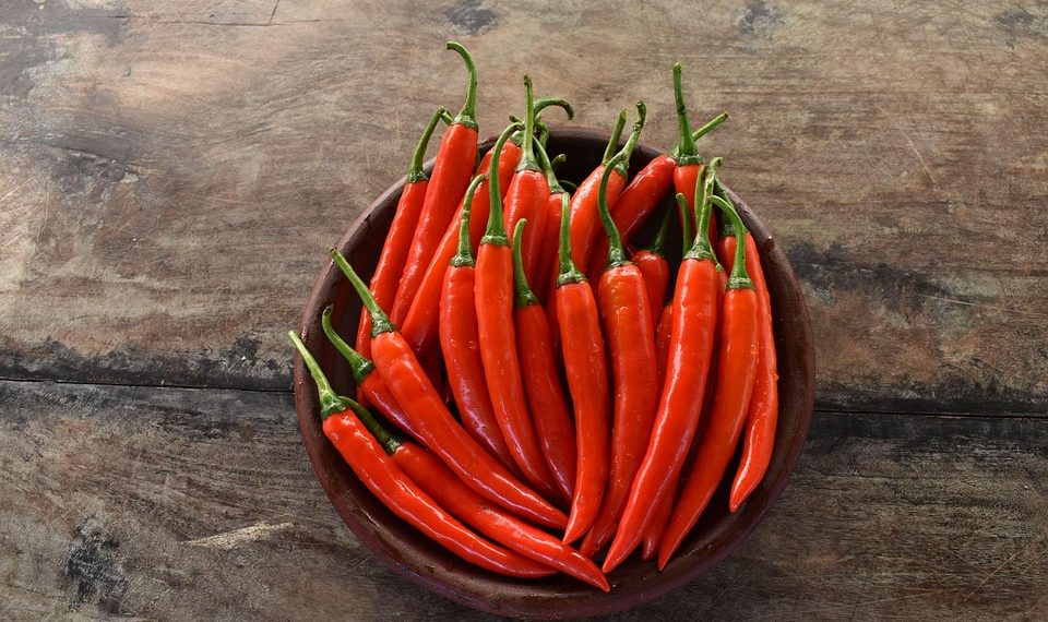 Red chili peppers in a bowl on a rustic wooden background.