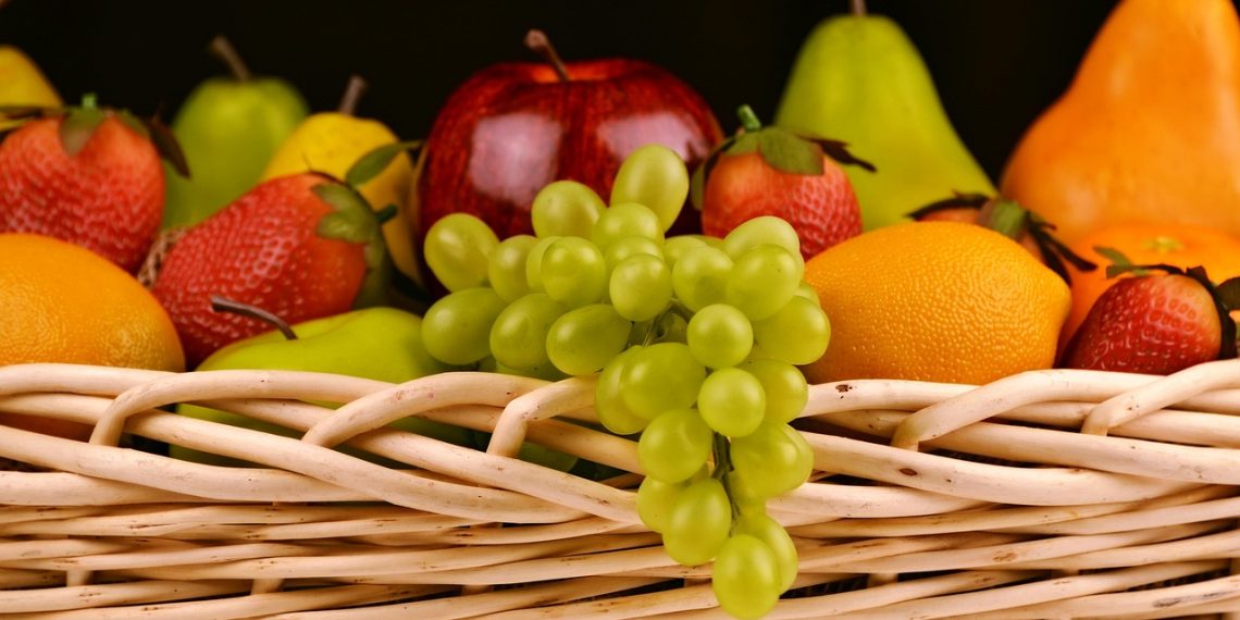 Mixed fruit basket with grapes, apple, pear, and strawberries arranged in a woven container.