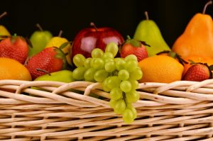 Mixed fruit basket with grapes, apple, pear, and strawberries arranged in a woven container.