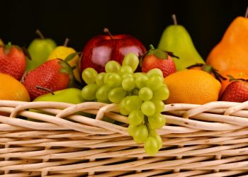 Mixed fruit basket with grapes, apple, pear, and strawberries arranged in a woven container.