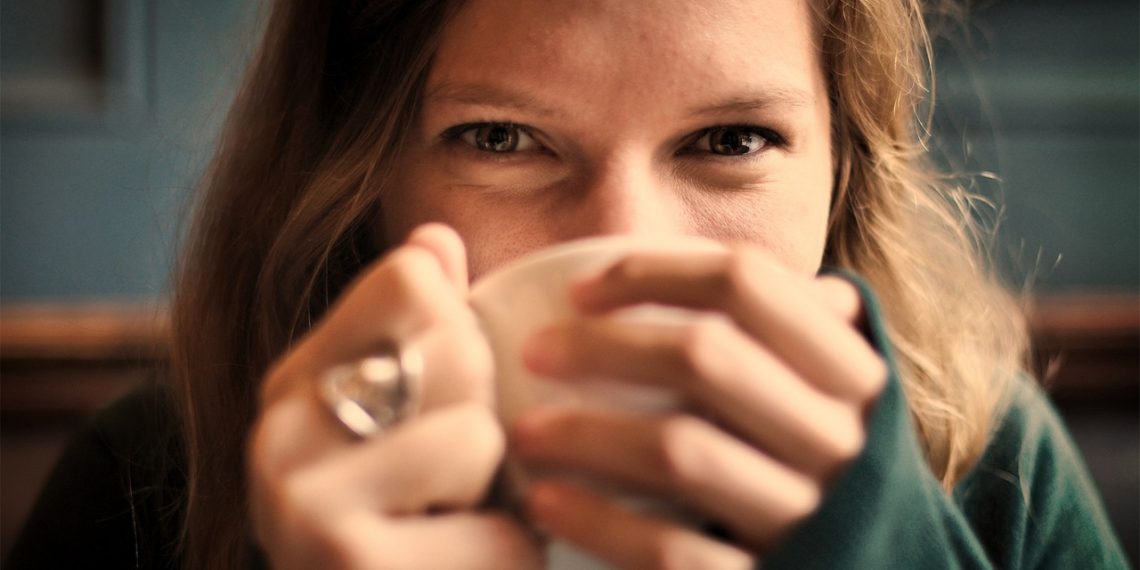 Woman enjoying a warm drink, smiling behind cup.