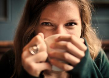 Woman enjoying a warm drink, smiling behind cup.