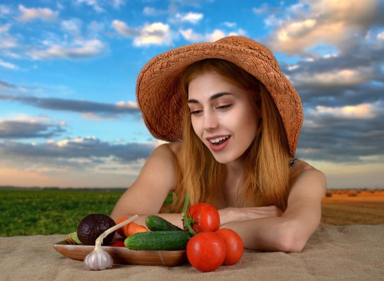 Woman admiring fresh vegetables at a table in a field.