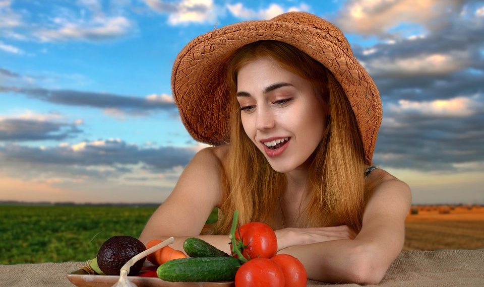 Woman admiring fresh vegetables at a table in a field.