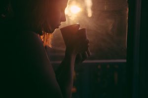 Woman enjoying morning coffee by window with sunrise.