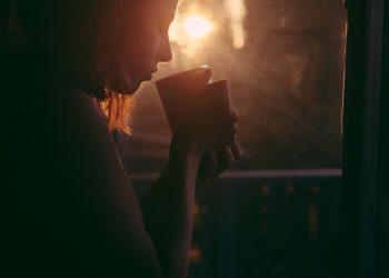 Woman enjoying morning coffee by window with sunrise.