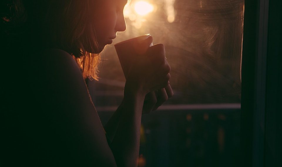 Woman enjoying morning coffee by window with sunrise.
