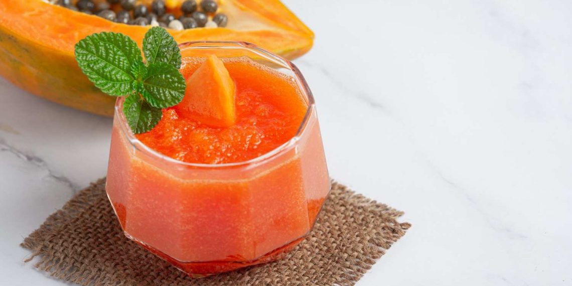 Papaya smoothie garnished with mint leaves placed next to a halved papaya.