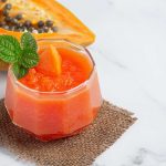 Papaya smoothie garnished with mint leaves placed next to a halved papaya.