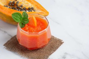 Papaya smoothie garnished with mint leaves placed next to a halved papaya.