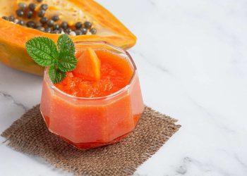 Papaya smoothie garnished with mint leaves placed next to a halved papaya.