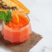 Papaya smoothie garnished with mint leaves placed next to a halved papaya.