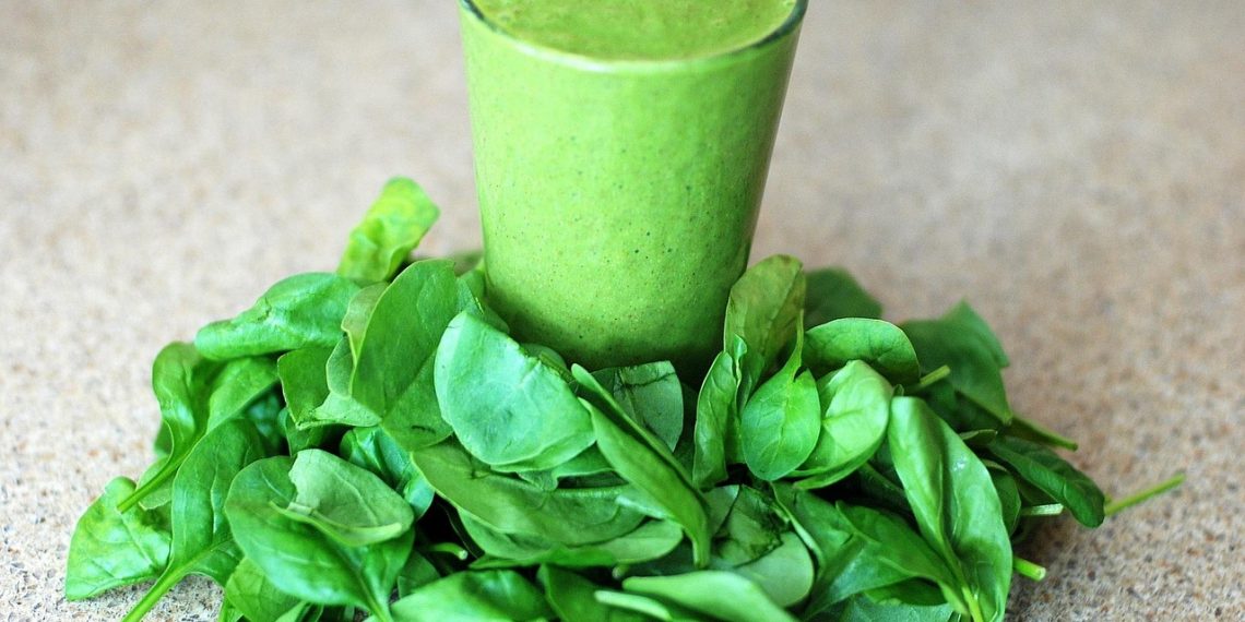 Spinach smoothie surrounded by fresh spinach leaves.