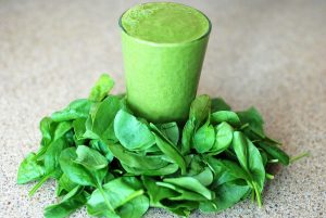 Spinach smoothie surrounded by fresh spinach leaves.