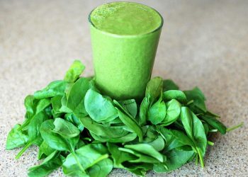 Spinach smoothie surrounded by fresh spinach leaves.