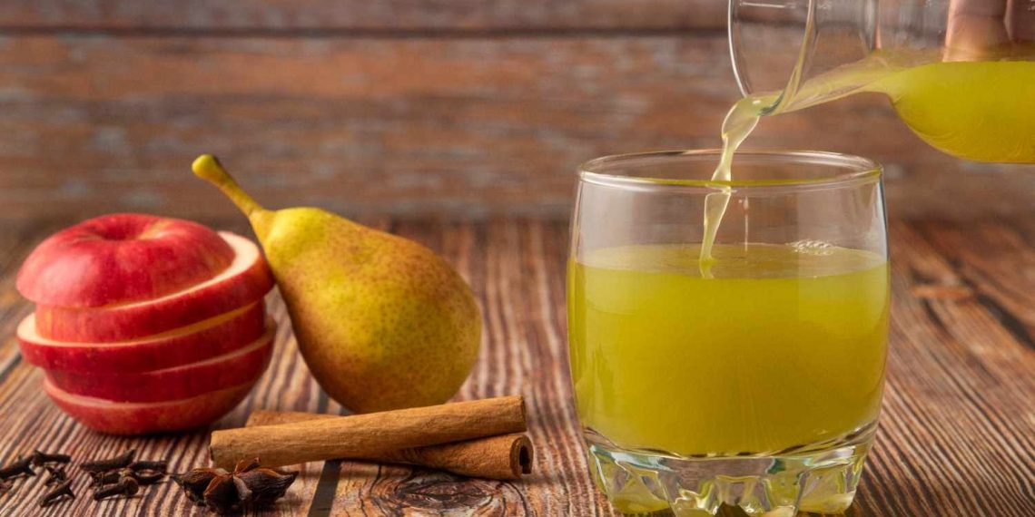 Pouring fresh pear juice with sliced apple and cinnamon.