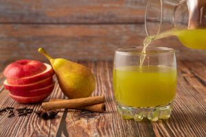 Pouring fresh pear juice with sliced apple and cinnamon.
