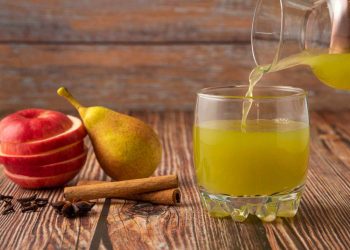 Pouring fresh pear juice with sliced apple and cinnamon.