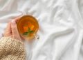 Hand holding a cup of herbal tea with mint leaves on a cozy sweater.