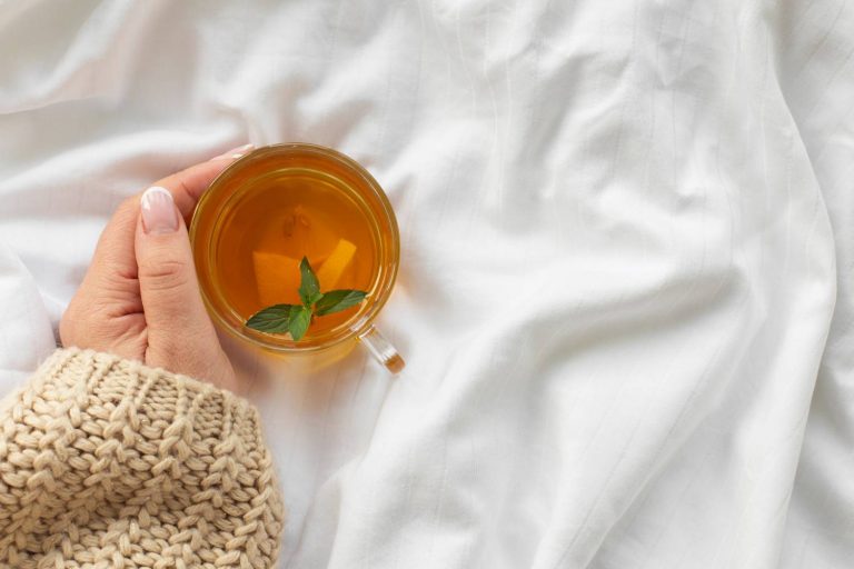Hand holding a cup of herbal tea with mint leaves on a cozy sweater.