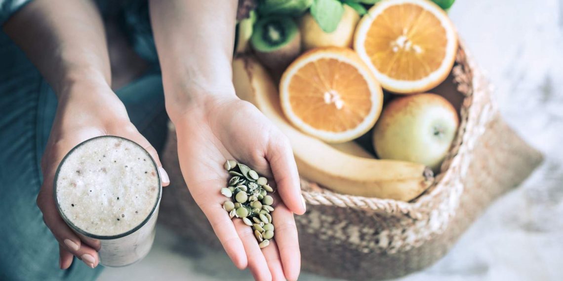 Smoothie and seeds held above a basket of fresh fruits.