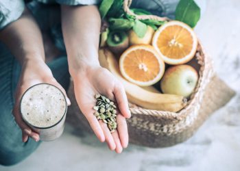 Smoothie and seeds held above a basket of fresh fruits.