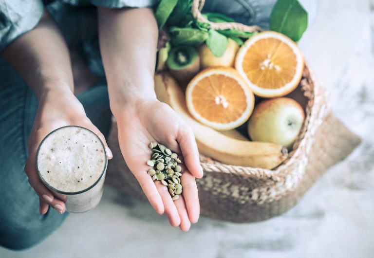 Smoothie and seeds held above a basket of fresh fruits.