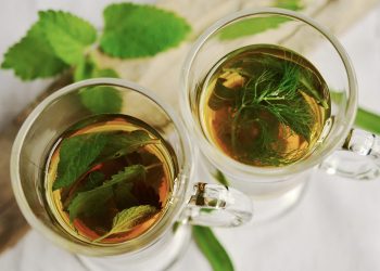 Two cups of herbal tea with fresh mint leaves floating.