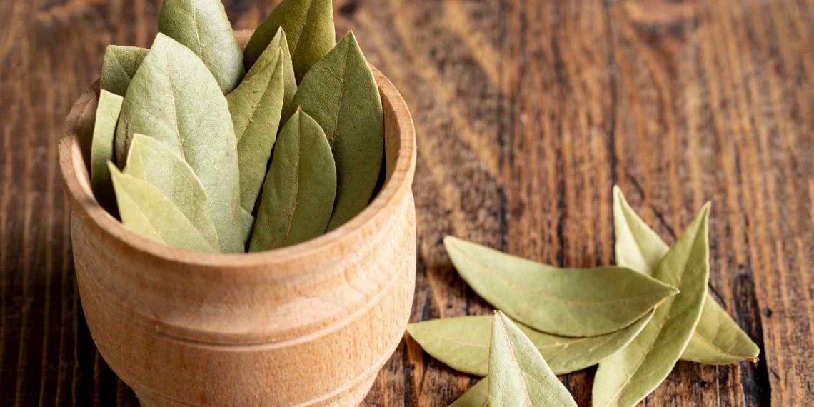 Dried bay leaves in a wooden bowl on a rustic wooden surface.