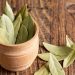 Dried bay leaves in a wooden bowl on a rustic wooden surface.