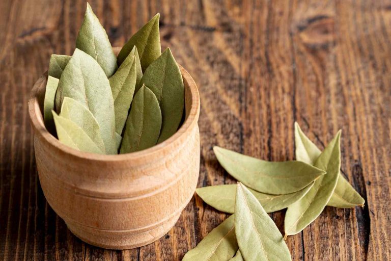 Dried bay leaves in a wooden bowl on a rustic wooden surface.
