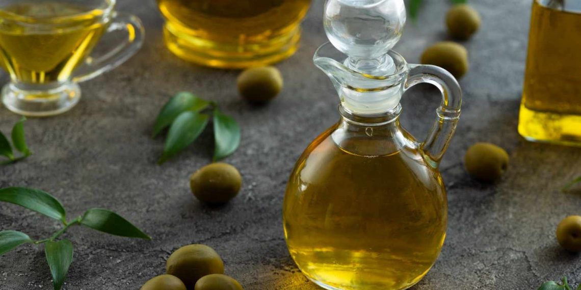Decanter of olive oil surrounded by olives and leaves.