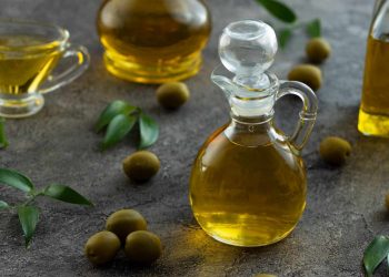 Decanter of olive oil surrounded by olives and leaves.