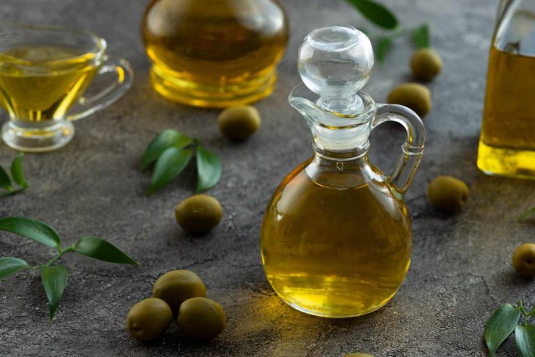 Decanter of olive oil surrounded by olives and leaves.
