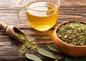 Cup of moringa tea beside a bowl of dried moringa leaves on a wooden table.