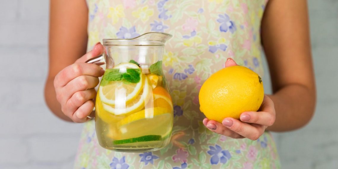 Woman holding lemon and pitcher of citrus water