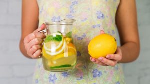 Woman holding lemon and pitcher of citrus water